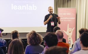 Mann mit Mikrofon spricht vor Publikum. Leinwand zeigt "leanlab November 2025", Banner: "Von der Idee zum Geschäftsmodell in 48 Stunden".
