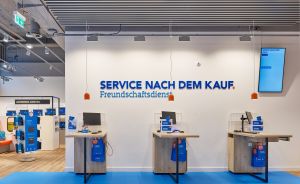 Servicebereich mit drei Holztresen, blauem Boden und Wandschriftzug „Service nach dem Kauf. Freundschaftsdienst".