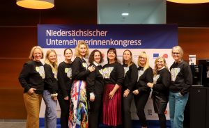 Neun Personen in schwarzen Sweatshirts stehen vor einem Banner „Niedersächsischer Unternehmerinnenkongress".