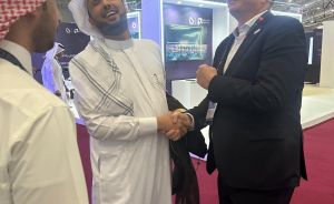 Zwei Männer geben sich die Hand auf einer Messe; einer trägt traditionelle arabische Kleidung, der andere einen Anzug.