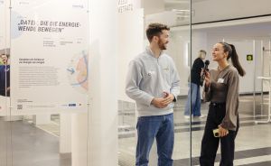 Zwei Personen stehen vor einem Ausstellungsplakat „Daten, die die Energiewende bewegen". Eine hält ein Mikrofon.
