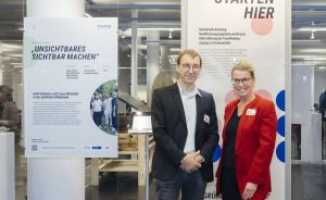 Zwei Personen stehen vor Ausstellungstafeln mit deutschem Text „Unsichtbares sichtbar machen" und „Ideen starten hier".