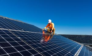 Techniker in orangefarbener Schutzkleidung und weißem Helm installiert Solarpanele auf einem Hausdach.