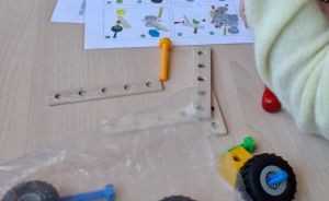 Zwei Personen bauen ein Konstruktionsspielzeug zusammen. Auf dem Tisch liegen Bauteile, Räder und eine Anleitung.