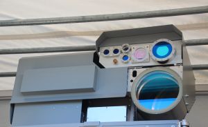 Graues militärisches Gerät mit mehreren optischen Linsen und Sensoren, montiert unter einem Vordach.