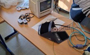 Medizinischer Monitor, Blutdruckmanschette, Pulsoximeter und Kabel auf einem Holztisch in einem Raum mit Waschbecken.