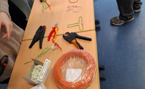 Holztisch mit Elektrowerkzeug: Abisolierzangen, Kombizange, Kabelrollen in Orange und Gelb sowie Anschlussklemmen.