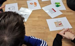 Mehrere Personen sitzen an einem Holztisch, auf dem viele bedruckte Bildkarten mit Illustrationen verteilt liegen.