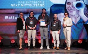 Fünf Personen auf einer Bühne, einer hält eine Urkunde. Im Hintergrund: „Preiskategorie Next Mittelstand".
