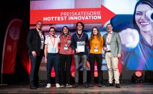 Sechs Personen stehen auf einer Bühne vor einer Leinwand mit der Aufschrift „Preiskategorie Hottest Innovation".