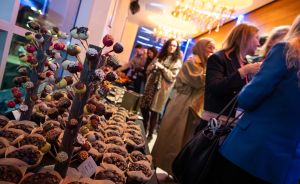 Marktstand mit Cake Pops und Pralinenpralinen in Papier, dahinter Personengruppe in einem beleuchteten Innenraum.
