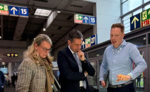 Drei Personen betrachten ein beleuchtetes Stadtplanungsmodell mit farbigen Gebäuden auf einer Messe.