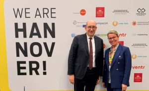 Zwei Personen stehen vor einem gelben Banner mit der Aufschrift „We Are Hannover" mit Stadtsilhouette und Sponsor-Logos.