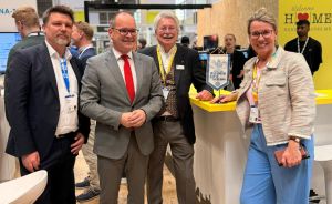 Vier Personen stehen lächelnd an einem Messestand mit der Aufschrift „Welcome Home Hannover Messe".