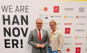 Zwei Personen stehen vor einem gelb-weißen Banner mit der Aufschrift „We Are Hannover!" auf einer Messe.