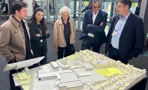 Fünf Personen stehen um ein weißes Architekturmodell eines Gebäudekomplexes auf einem schwarzen Sockel mit „Kubitur"-Logo.