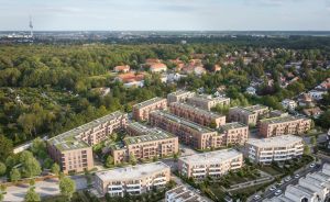 Luftaufnahme eines modernen Wohnquartiers mit mehrgeschossigen Backsteingebäuden, Grünanlagen und Balkonen, umgeben von Bäumen.