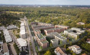 Luftbild eines Wohnquartiers mit mehrstöckigen Gebäuden, begrünten Dächern, Straßen und umgebenden Wäldern.