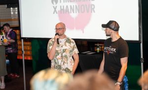 Zwei Männer stehen vor einer Leinwand mit der Aufschrift „Fireabend x Hannovr". Einer spricht ins Mikrofon.