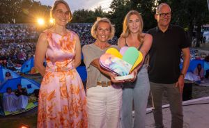 Drei Frauen und ein Mann auf der Bühne. Publikum im Hintergrund.