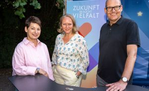 Zwei Frauen und ein Mann am Tresen. Im Hintergrund ein Rollup von Zukunft braucht Vielfalt.
