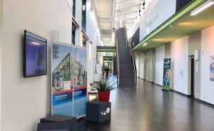 Heller Gebäudeflur mit dunklem Fliesenboden, Rollup-Banner mit Aufschrift „Hannover", Treppe und Galerie im Hintergrund.