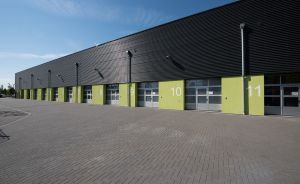 Industriegebäude mit schwarzer Fassade, grün-gelben Sektionen nummeriert 8–11, große Glastüren, gepflasterter Vorplatz.