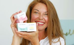 Lächelnde Frau hält drei kleine Kosmetikprodukte der Marke "Ombelle" in die Kamera, darunter eine SPF 30 Creme.