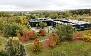 Luftaufnahme eines modernen Bürogebäudes, umgeben von herbstlich gefärbten Bäumen in Rot, Orange und Gelb.