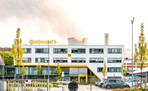 Mehrstöckiges Bürogebäude mit Continental-Logo, Parkplatz davor, Bäume, Rauchsäule im Hintergrund.