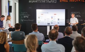 Präsentation beim KPMG Smart Start Award: Referent vor Leinwand, Publikum von hinten, Schriftzüge an schwarzer Wand.