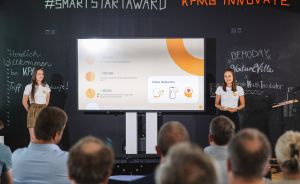 Zwei Frauen präsentieren vor Publikum beim #SmartStartAward von KPMG Innovate eine Folie mit Statistiken.