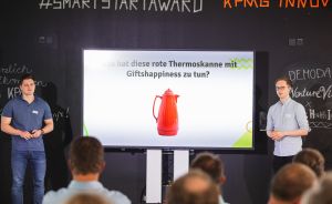 Zwei Männer präsentieren vor Publikum eine Folie mit roter Thermoskanne beim #SmartStartAward von KPMG.