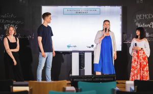 Vier Personen stehen auf einer Bühne vor einer Leinwand mit der Aufschrift „Digitaler Livestream Demoday".