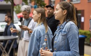Mehrere Personen in Jeansjacken stehen draußen. Eine Frau hält eine Flasche Bionade in der Hand.