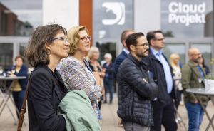 Gruppe von Personen steht vor einem Gebäude mit der Aufschrift „Cloud Projekt" und schaut in eine Richtung.