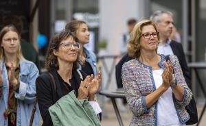 Mehrere Personen stehen im Freien und applaudieren. Zwei Frauen mit Brille stehen im Vordergrund.