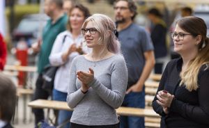 Mehrere Personen stehen im Freien und klatschen. Im Vordergrund eine junge Frau mit Brille und blonden Haaren.