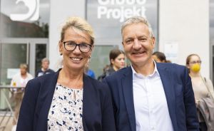 Zwei Personen in blauen Blazern lächeln vor einem Gebäude mit der Aufschrift „Cloud Projekt".