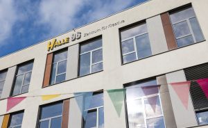Gebäudefassade mit Schriftzug „Halle 96 – Zentrum für Kreative", bunten Wimpelketten und blauem Himmel.