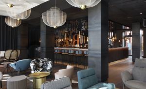 Moderne Hotellobby mit weißen Hängeleuchten, verschiedenfarbigen Sesseln, Goldtischen und einer Bar mit Typografie-Wandgestaltung.