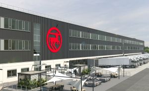 Modernes Industriegebäude mit rotem Logo, Parkplatz mit LKW-Stellplätzen und überdachten Außenbereichen.