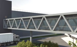 Metallische Fußgängerbrücke mit Glasfassade verbindet zwei Industriegebäude; darunter ein weißer LKW-Sattelzug.