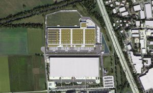 Luftbild zweier großer Industriegebäude mit begrüntem Dach, umgeben von Feldern, Straßen und Wohnbebauung.