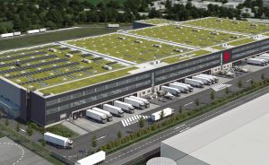 Luftbild eines großen Lagergebäudes mit Grün­dach, Solar­panels, Lade­rampen und geparkten LKW auf dem Firmen­gelände.