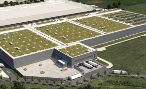 Luftbild eines großen Industriegebäudes mit begrüntem Flachdach, Laderampen und geparkten LKW auf dem Gelände.