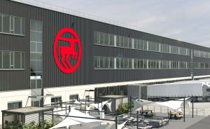 Modernes Industriegebäude mit grauer Fassade, rotem Firmenlogo, und Außenbereich mit Tischen, Stühlen und Sonnensegeln.