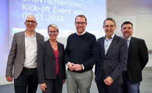 Fünf Personen stehen lächelnd vor einer Präsentation mit der Aufschrift „SMINT@Hannover Kick-off Event am 05.11.2022".
