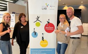 Vier Personen stehen lächelnd neben einem Regio Lab Roll-up-Banner in einem Gebäude.