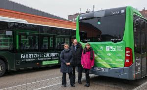 Drei Personen stehen vor zwei grünen ÜSTRA-Bussen. Aufschrift: „Fahrtziel: Zukunft! Wasserstoffregion Hannover."